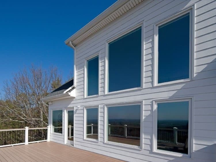 Large new windows across the back of a white home above a deck